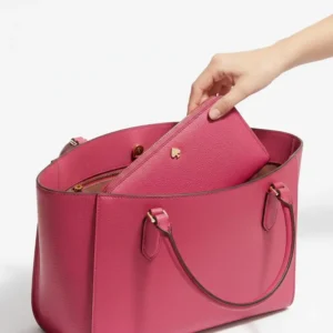 A kate spade large continental wallet being placed inside a large leather tote bag for daily use.