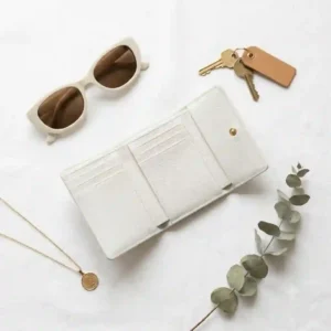 Elegant flat lay of a classic white wallet paired with sunglasses, keys, and summer fashion accessories.